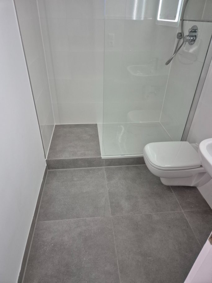 Badrenovierung Moderne Badezimmeransicht mit Dusche und WC auf grauem Boden.