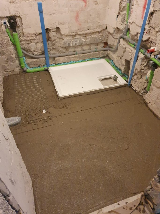 Badrenovierung Boden mit frischem Estrich, vorbereitet für eine Duschwanne und Installationsrohre.