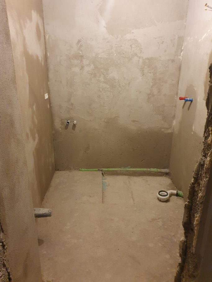Badrenovierung Rohbau eines Duschbereichs mit unverputzten Wänden und sichtbaren Rohren.