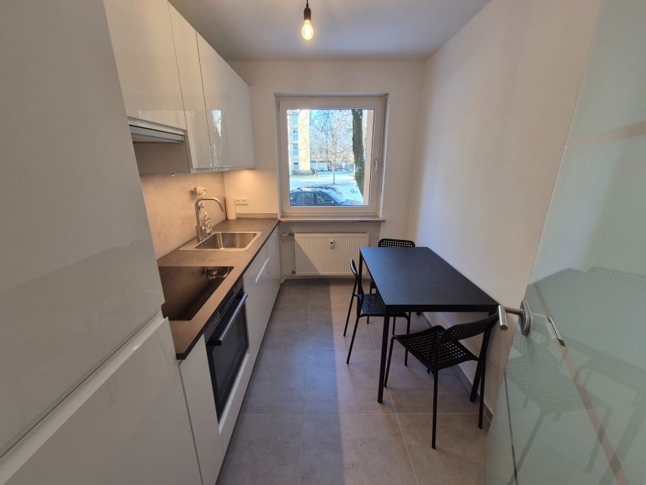Kleine moderne Küche mit Elektrogeräten, Tisch und Stühlen neben einem Fenster.