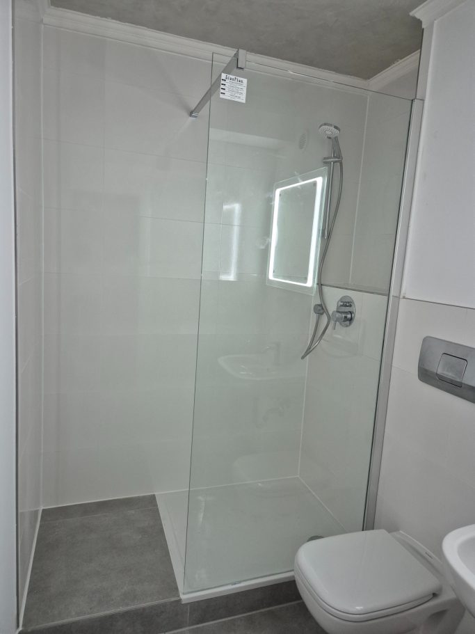 Badrenovierung Dusche mit gläserner Trennwand und modernen Sanitäranlagen, helle Fliesen.