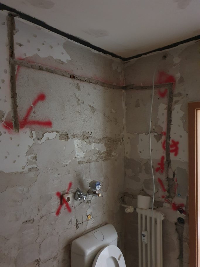 Badrenovierung Rohbau eines Badezimmers mit markierten Wänden und Rohrleitungen.