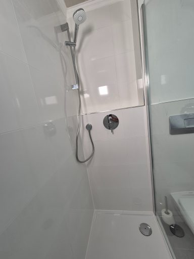 Moderne Dusche mit Glaswand und verchromtem Duschkopf in hellen Fliesen.